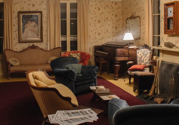 Living room of the summer residence with two sofas, two arm chairs, a piano and a fireplace.