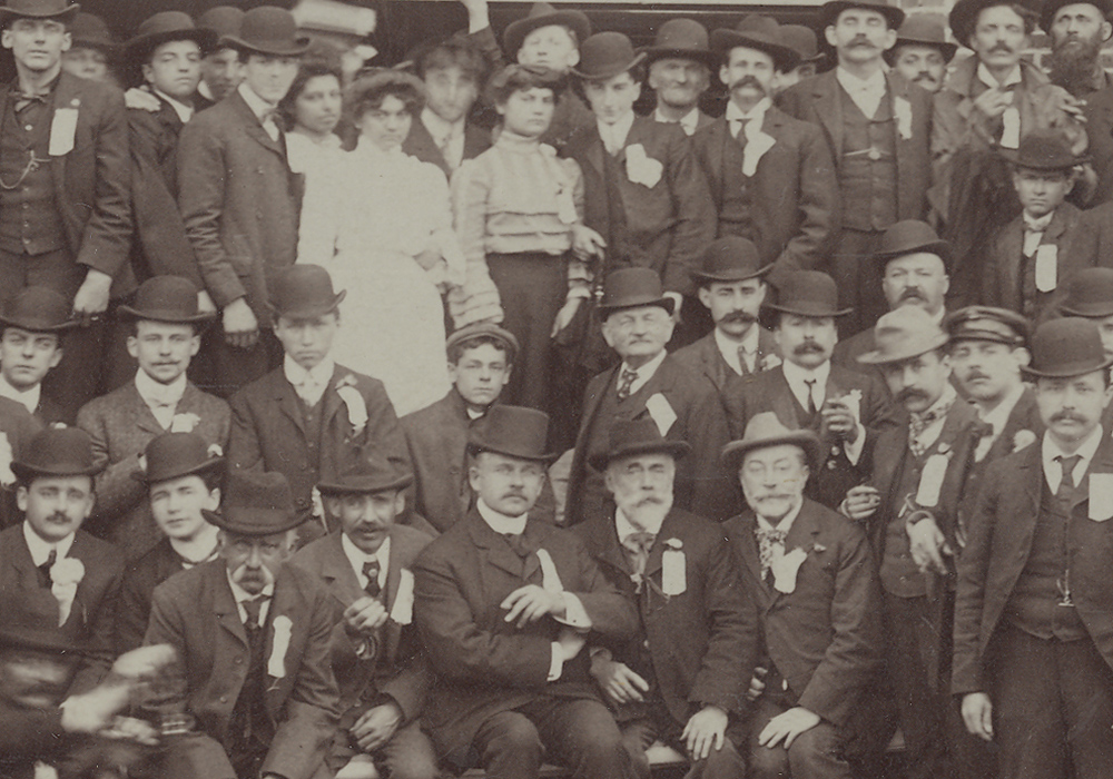 Sepia-tone photograph showing men and some women outside, in front of a paper mill.