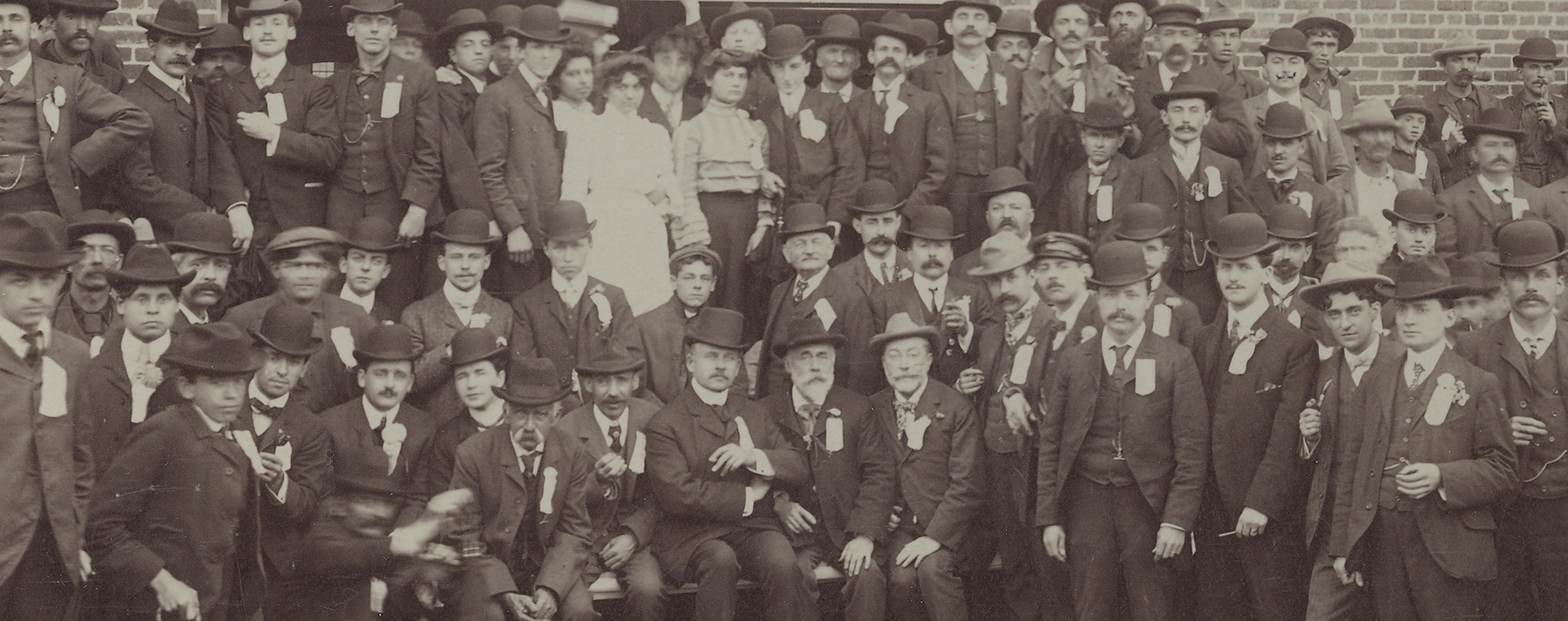 Sepia-tone photograph showing men and some women outside, in front of a paper mill.