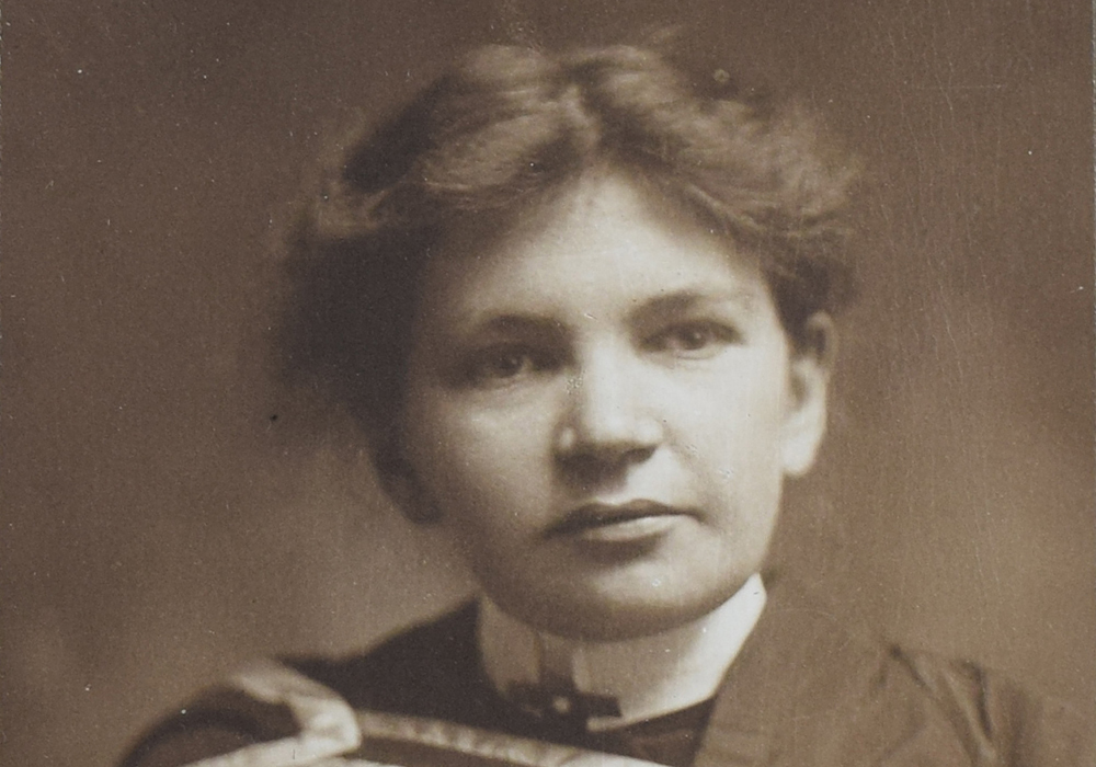 Black and white photograph of Maude Abbott as a young adult, from the waist up. She is wearing a graduation gown. Her dark hair is tied behind her head and she is looking slightly to her left.