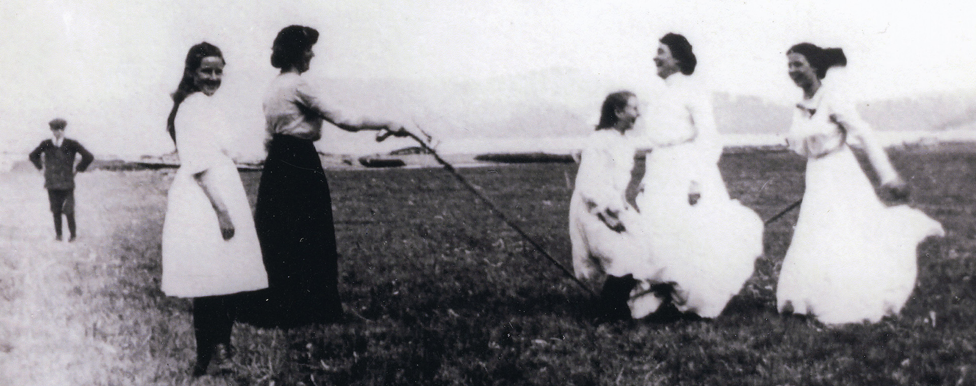 A black and white photograph of women skipping with a jump rope in a field.