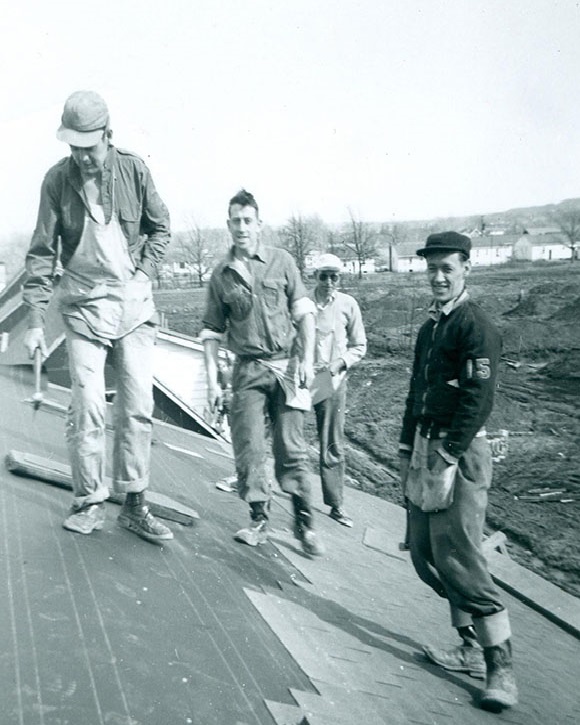 Black and white photograph of a group of four men on a roof .