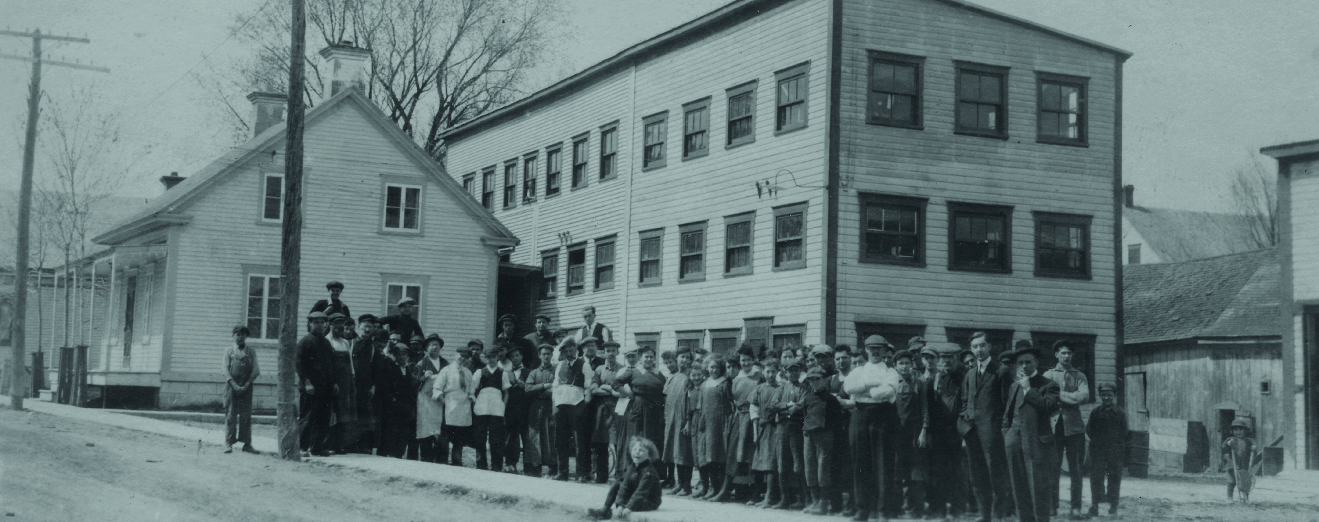 The picture shows employees assembles in front of the Charron factory. It is a three-story wooden structure, built behind a house on St-Antoine Street.