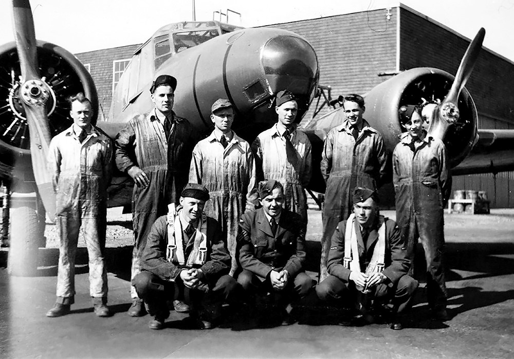 3 airmen and 6 mechanics in front of airplane and hanger.