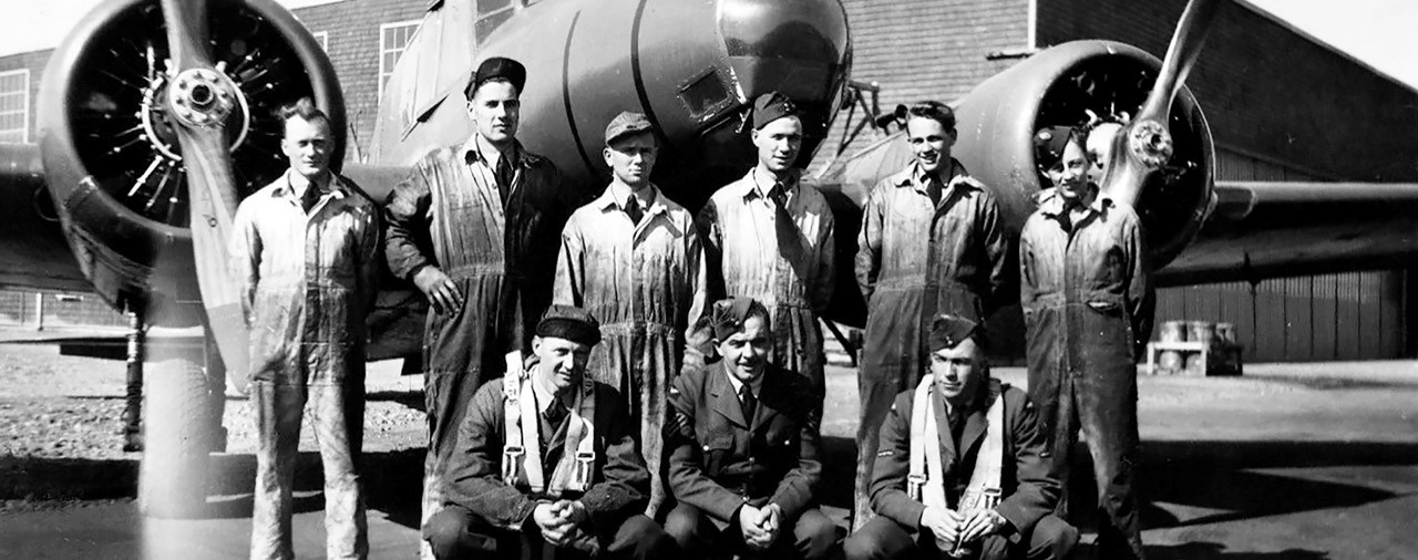 3 airmen and 6 mechanics in front of airplane and hanger.