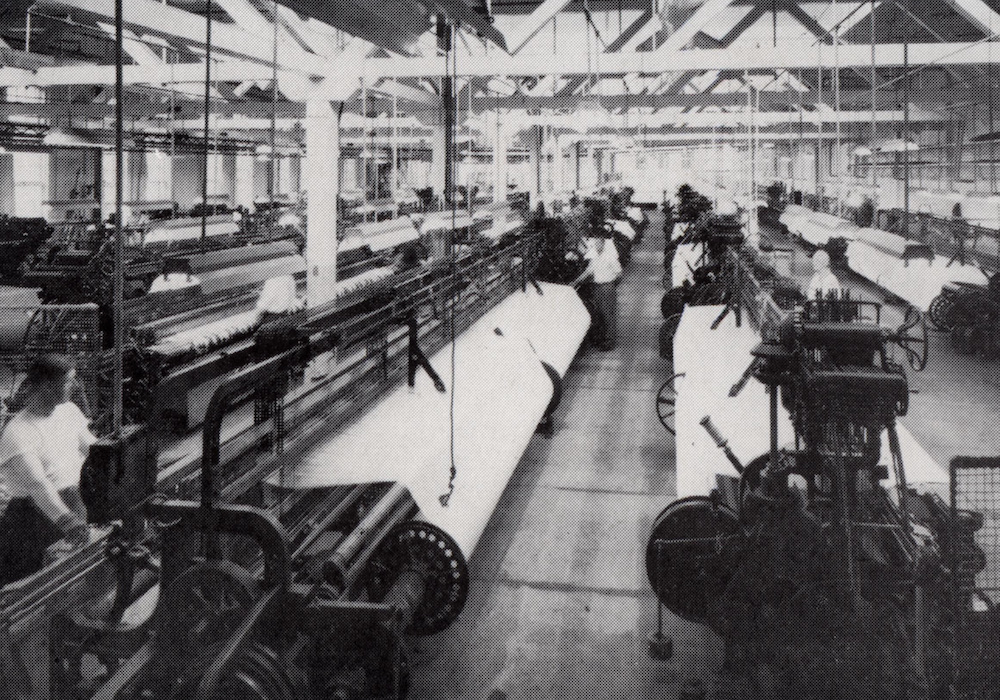 A factory floor with several rows of weaving machines.