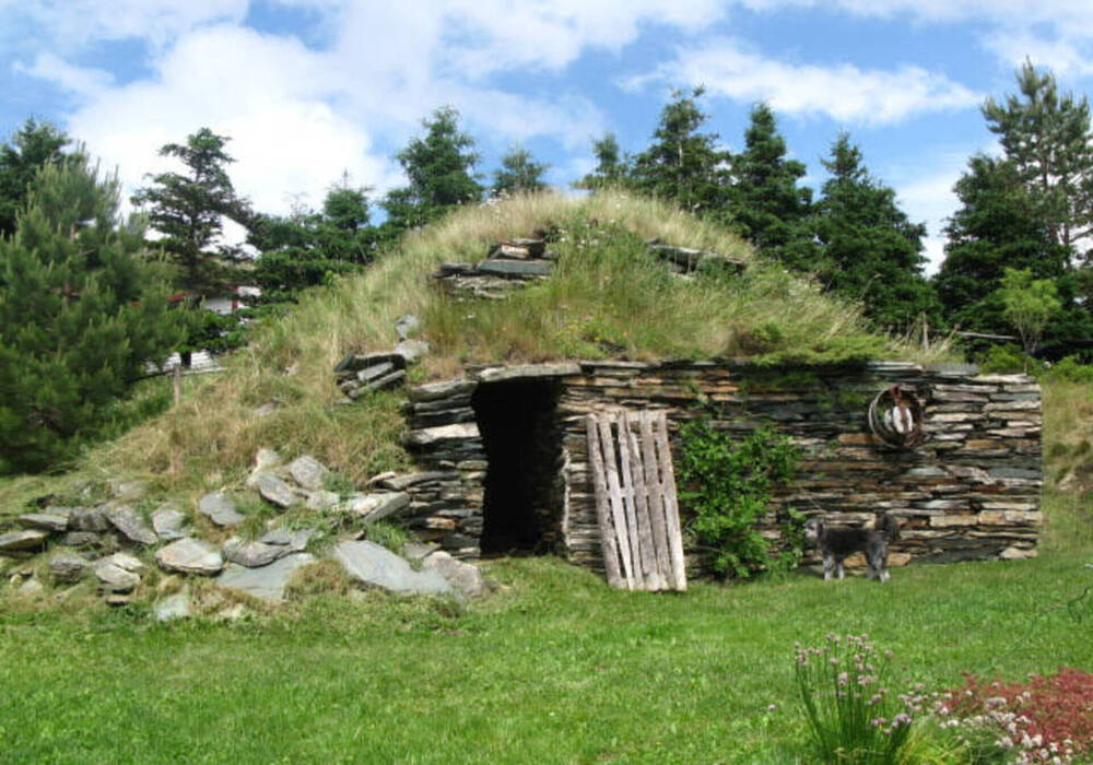 Exterior of a hillside root cellar with a stacked stone front and grass ontop.