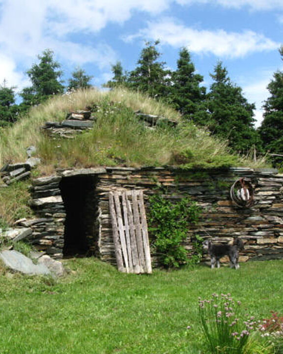 Exterior of a hillside root cellar with a stacked stone front and grass ontop.