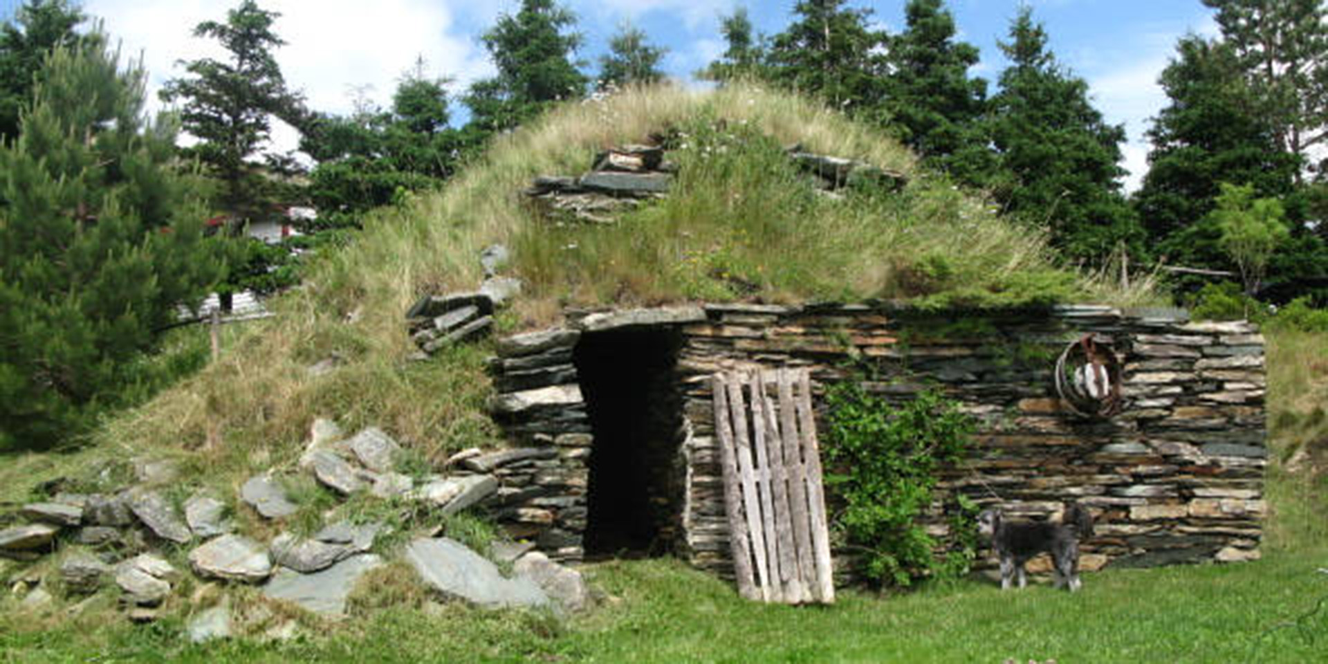 Exterior of a hillside root cellar with a stacked stone front and grass on top.