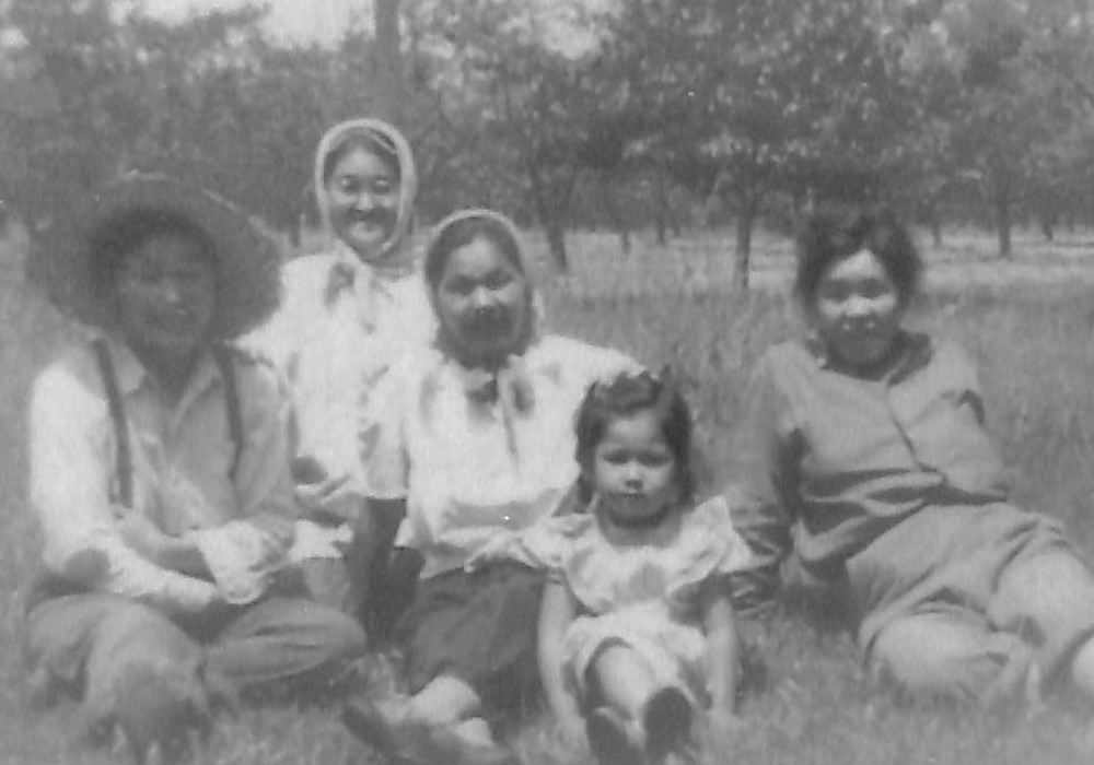 Four women and a young girl sitting in the grass in an orchard