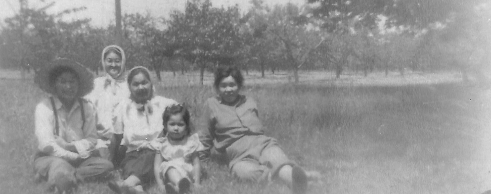 Four women and a young girl sitting in the grass in an orchard