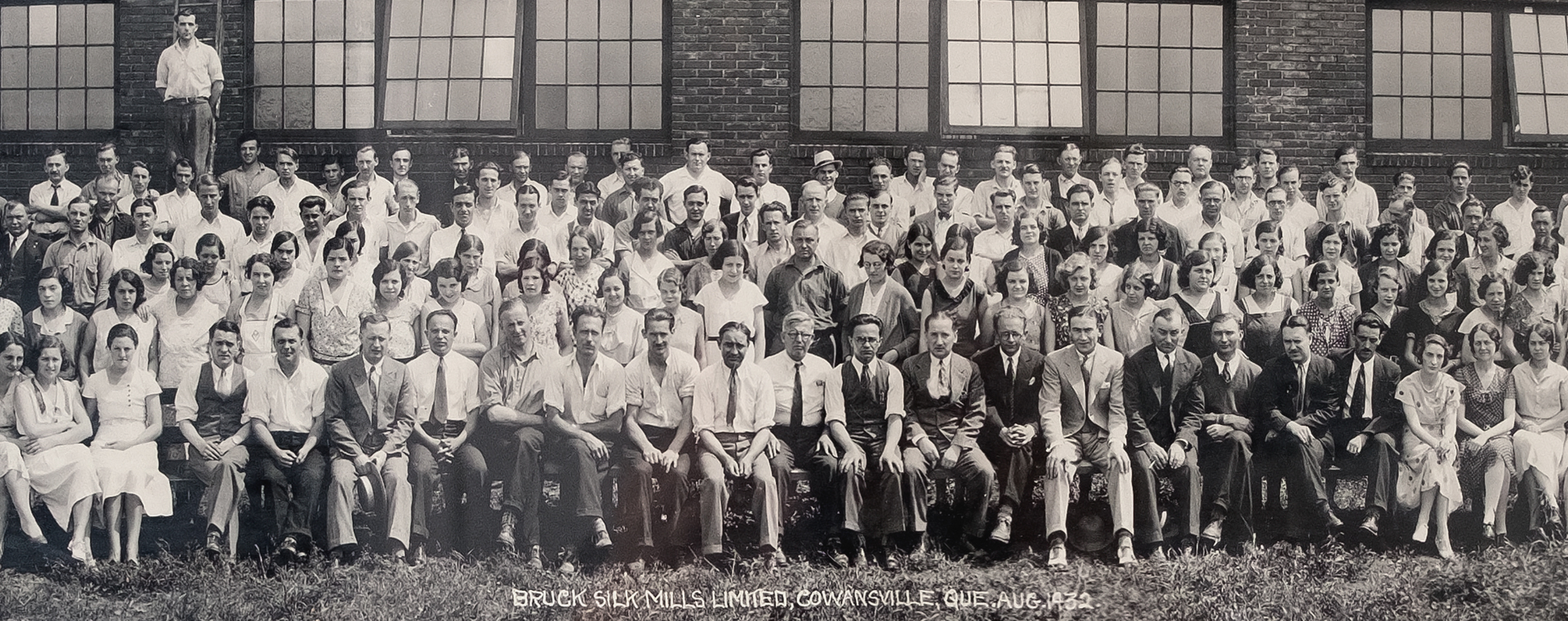 Black and white panoramic photo. A large number of employees and managers of the company pose in front of the factory on four rows.