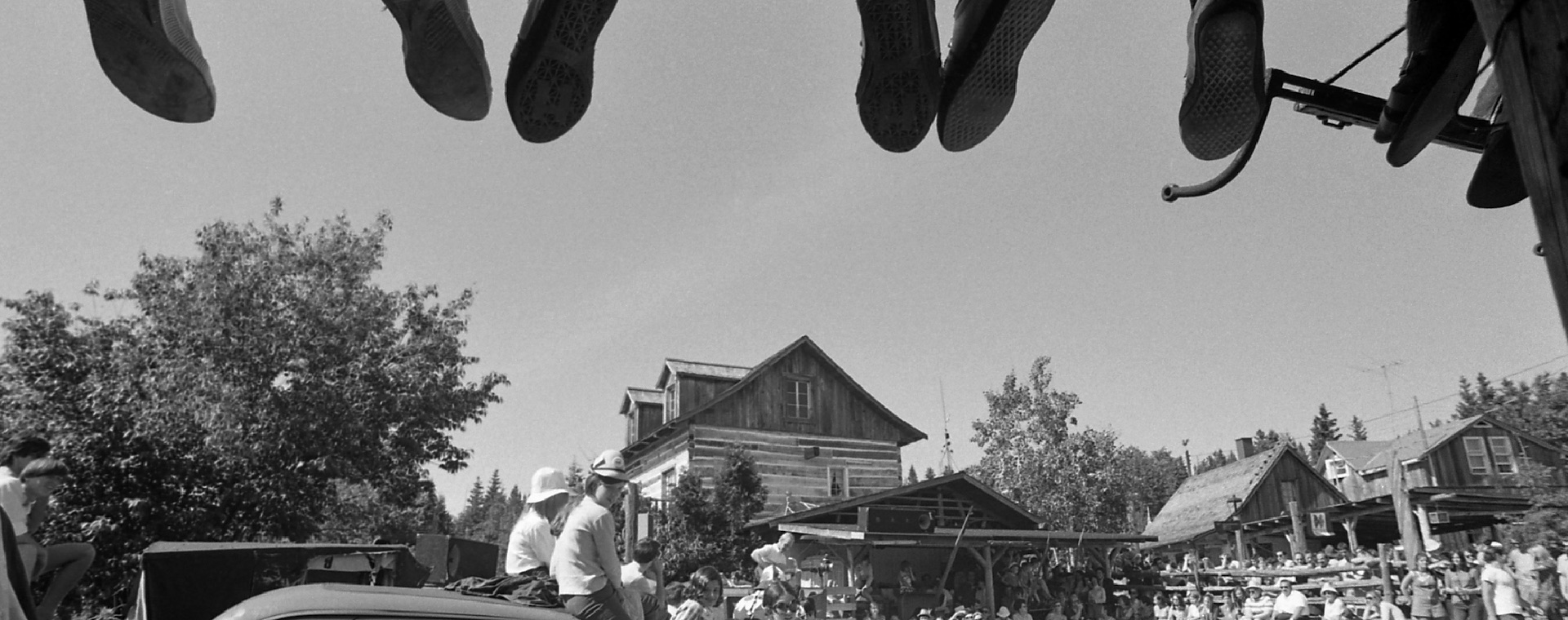 Black and white photo of about 100 spectators attending an outdoor performance at La Butte. At the top of the picture, the feet of people sitting on part of the roof of La Butte can be seen.