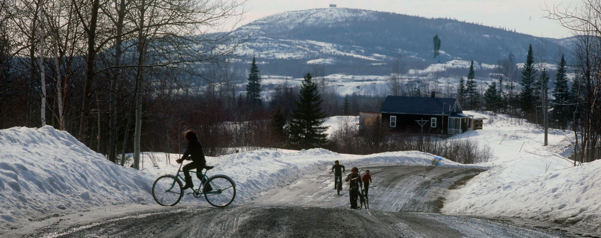 View of a landscape and a rural road in spring during the snow melt. Children riding their bikes.